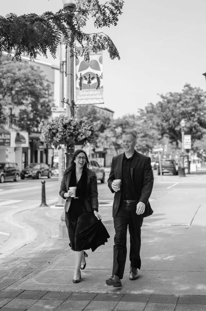 Two professionals walking and chatting on a city sidewalk, holding coffee cups.