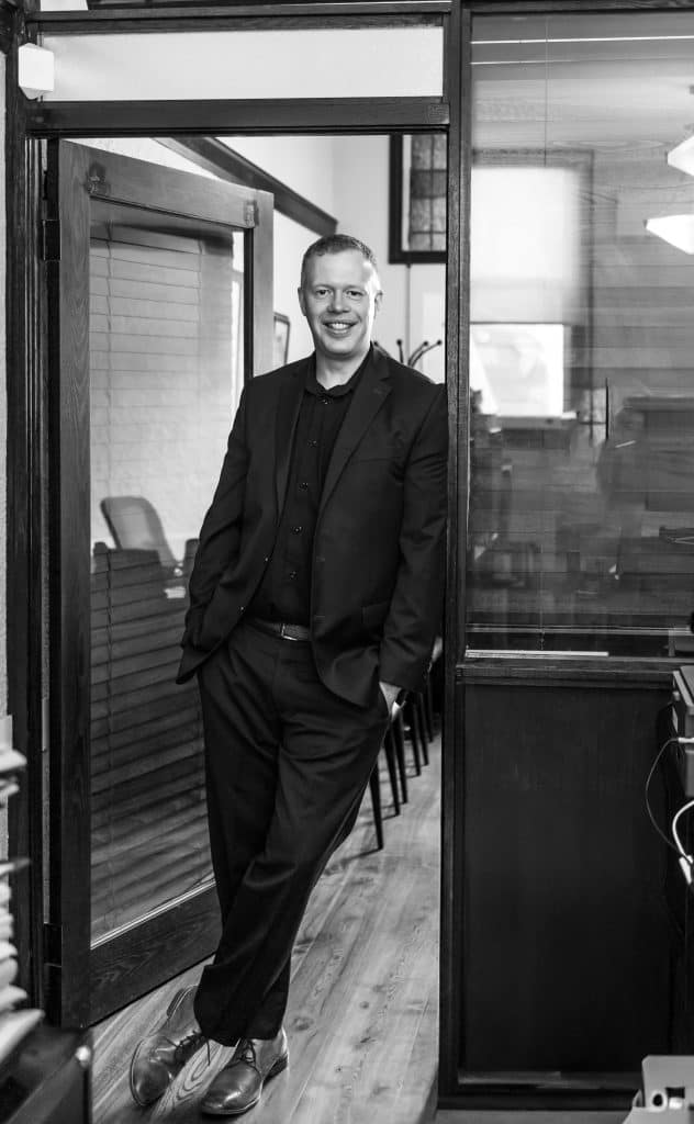 Business professional standing in office doorway, smiling confidently.